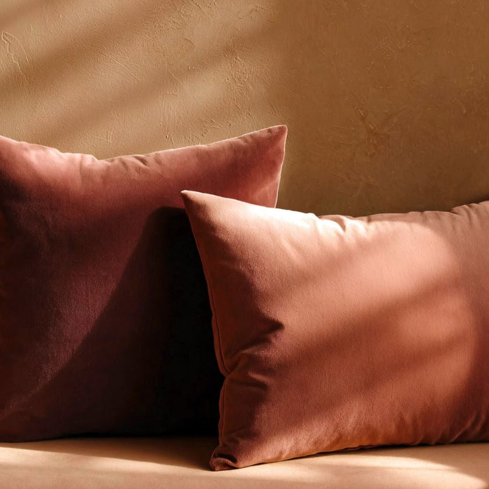 Two velvet throw pillows in warm terracotta tones on a beige sofa, soft sunlight accents.