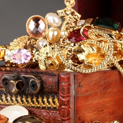 Open wooden chest filled with gold jewelry, gemstones, and pearls on display