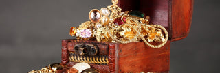 Open wooden chest filled with gold jewelry, gemstones, and pearls on display