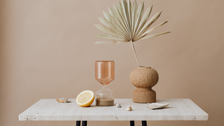 Modern hourglass sand timer with seashells, lemon slice, ceramic vase, and palm leaf on marble table