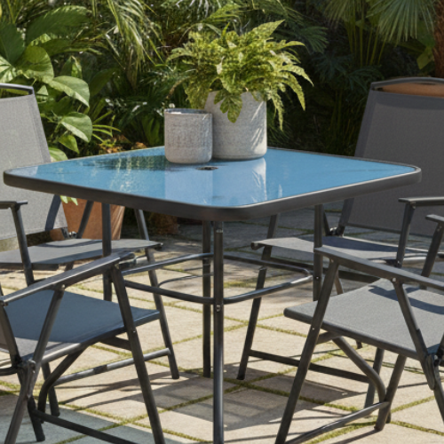 Modern outdoor patio set with four grey chairs, glass table, and potted plants in garden