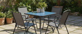 Modern outdoor patio set with four grey chairs, glass table, and potted plants in garden