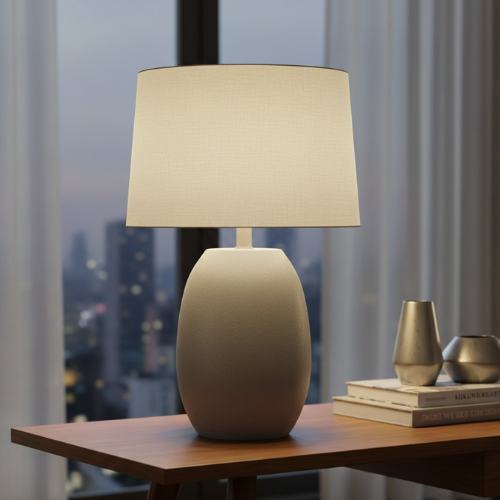 Modern table lamp with beige shade on wooden nightstand by window, city view at dusk