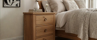 Wooden bedside table with drawers, lamp, books, and flower vase in a cozy bedroom setting