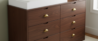 Modern wooden dresser with gold handles and white changing table top near a window