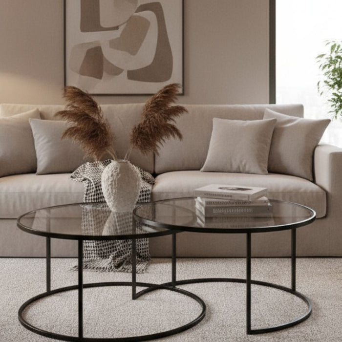 Modern living room with beige sofa, decorative pillows, glass coffee tables, and indoor plants