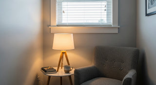 Cozy reading nook with armchair, side table, books, mug, and tripod table lamp by a window