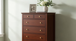Wooden chest of drawers with brass knobs, vase of white flowers, and framed photo on top
