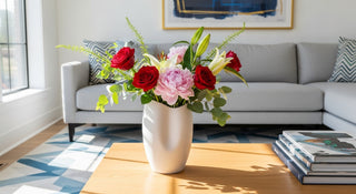 Modern living room with a white vase of red roses, lilies, and peonies on a wooden coffee table