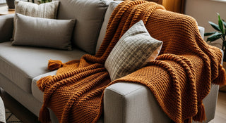 Cozy orange knit throw blanket with tassels on a modern grey sofa with accent cushions