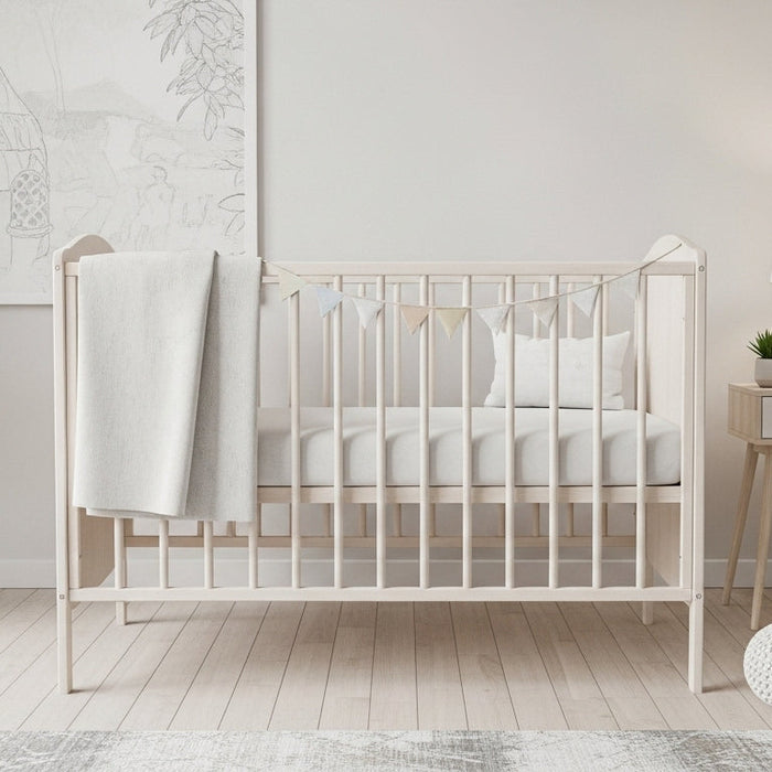Modern nursery room with light wood crib, white blanket, indoor plant, and neutral decor