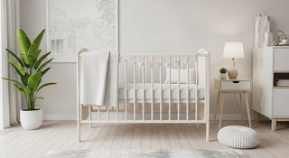 Modern nursery room with light wood crib, white blanket, indoor plant, and neutral decor