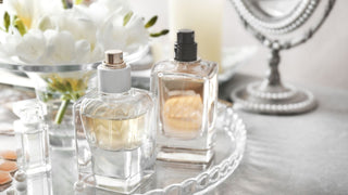 Elegant glass perfume bottles on mirrored tray with white flowers and pearls