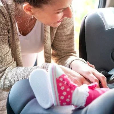 Smiling baby secured in a car seat with a woman adjusting the harness inside a vehicle.