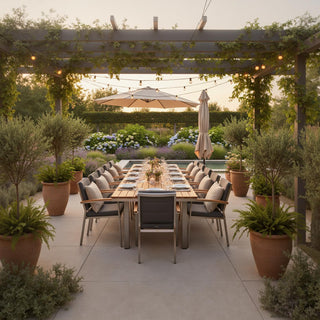 Outdoor dining area with wooden table, cushioned chairs, pergola, and garden plants at sunset