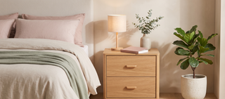 Two drawer bedside table with a lamp beside a bed in a calm, elegant bedroom.