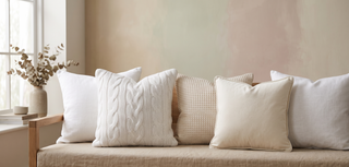 Range of white cushions in soft textures on a pastel backdrop.