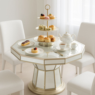 Elegant tea set with pastries and scones on mirrored table, white chairs, bright room