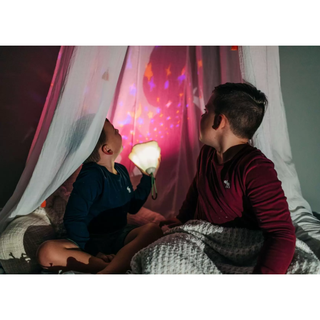 Two kids in a cozy bed tent watching colorful star and moon light projector at night