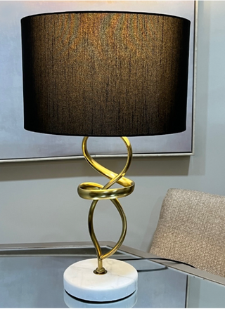 Gold and marble table lamp on glass desk beside upholstered chair.