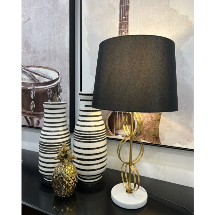 Gold and black table lamp next to striped vases and pineapple ornament.