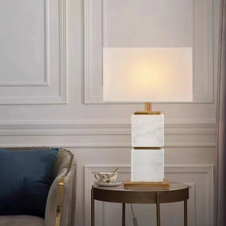 White marble table lamp on round side table beside velvet armchair in neutral living room.