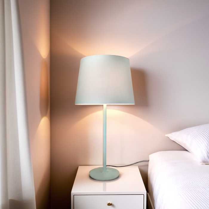 White metal Newport Lamp on bedside table in modern bedroom casting soft glow.