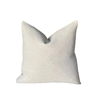A square throw pillow in a light oatmeal beige fabric, featuring a central diamond-shaped pleated design that creates a V-shape at the top, shown against a plain white background.