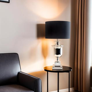 Paddington Silver Lamp beside dark armchair casting warm light with black shade and reflective silver base.
