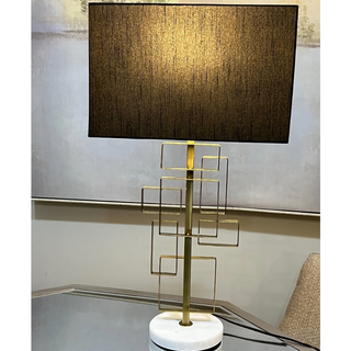 Metal square-frame gold stand table lamp with black shade on console.