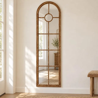 Arch wood trim panelled elongated mirror in bright hallway beside glazed door and bench