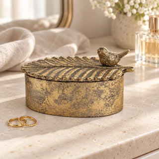 Avian elegance oval trinket box on travertine vanity beside gold rings and perfume