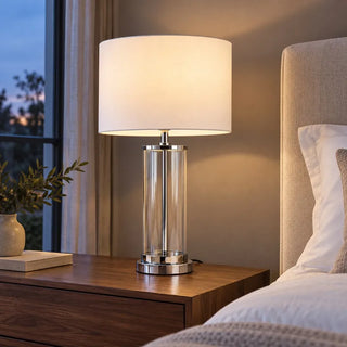 Chrome glass lamp lit on walnut bedside table beside upholstered headboard