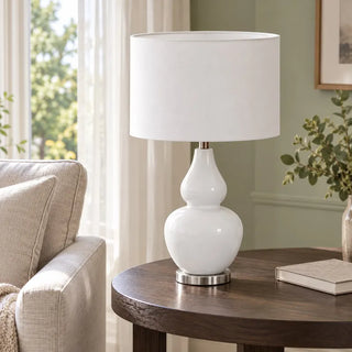 Coastal white classic table lamp on round dark wood side table beside linen armchair