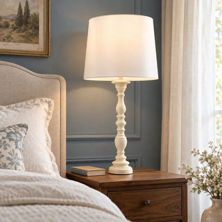 Country creamy table lamp on walnut bedside table beside linen headboard