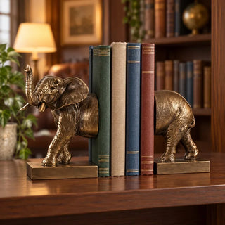 Elephant bookend set holding linen books on walnut shelf in lamp lit study