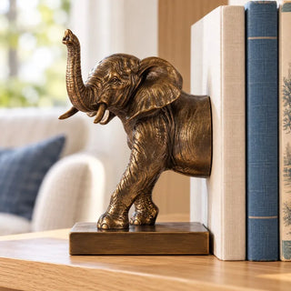 Elephant bookend set trunk half close up against books on oak shelf near cream sofa