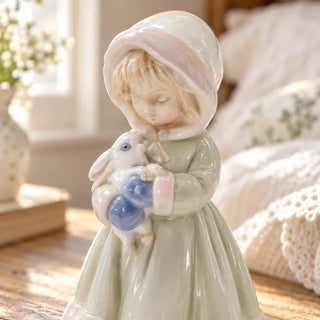 Girl holding rabbit figurine close up of pink trimmed bonnet and bunny in blue outfit