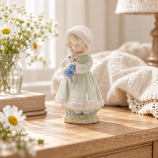 Girl holding rabbit figurine on wooden side table beside daisies in glass vase