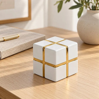 Gold banded ceramic cube decor on oak desk beside linen notebook and pen