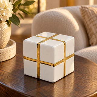 Gold banded ceramic cube decor on round timber side table beside cream boucle sofa