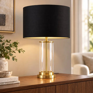 Gold plated glass lamp lit on walnut sideboard beside eucalyptus vase and armchair