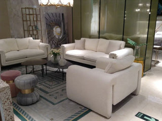 Modern living room with white sofas, round ottomans, glass coffee tables, and contemporary decor