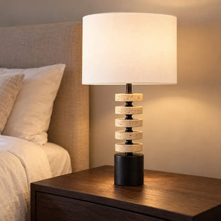 Kent marble lamp and shade lit on dark timber bedside table beside linen headboard