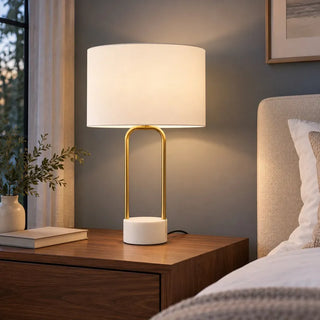Luna arc ceramic lamp lit on walnut bedside table beside upholstered headboard