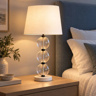 Marina sand glass lamp lit on oak bedside table beside blue upholstered headboard