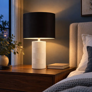 Norman ceramic lamp lit at night on walnut bedside table beside linen headboard