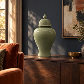 Oasis teal ceramic jar on walnut sideboard against navy wall beside rust armchair