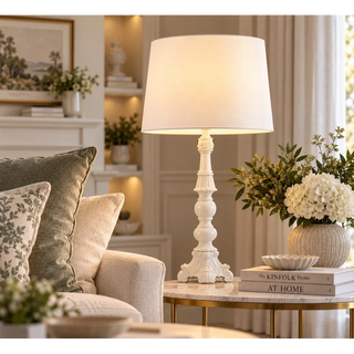 Ornate candlestick lamp on marble side table beside cream sofa and white hydrangeas