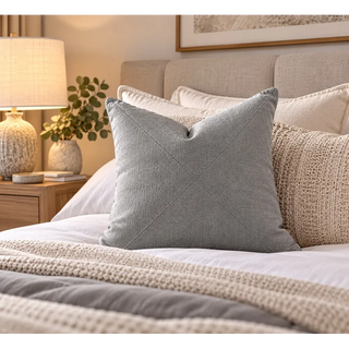 Pebble grey textured cushion on white bedding beside oak bedside table and lamp